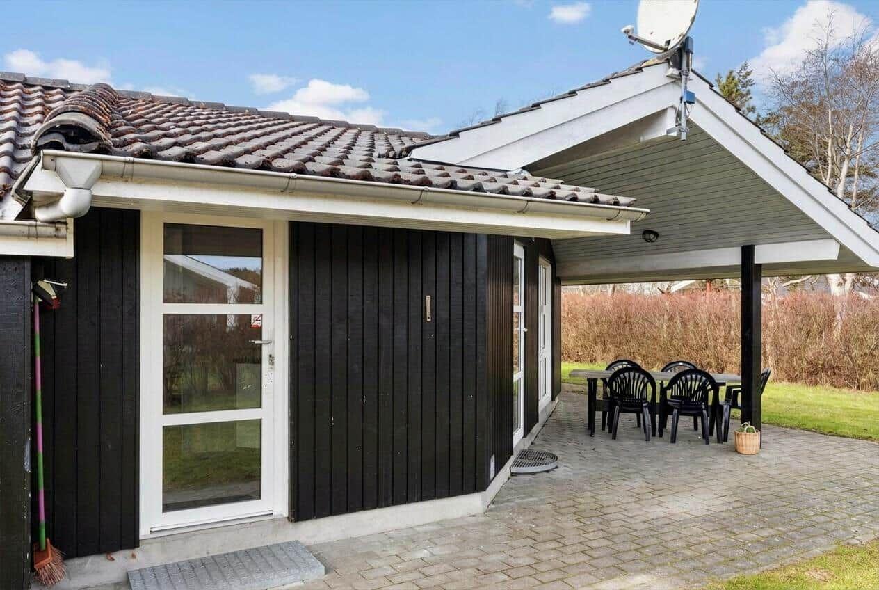 Haus mit Terrasse, Tisch und Stühlen, Satellitenschüssel und Ziegeldach.