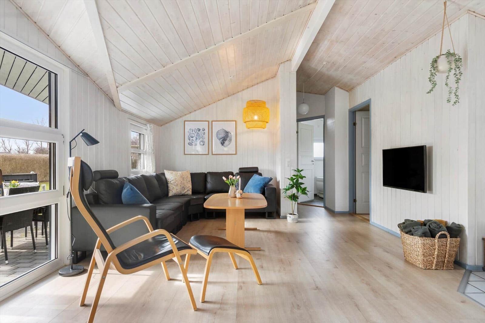 Wohnzimmer mit Sofa, Esstisch, TV und Holzboden. Fensterblick auf Terrasse.
