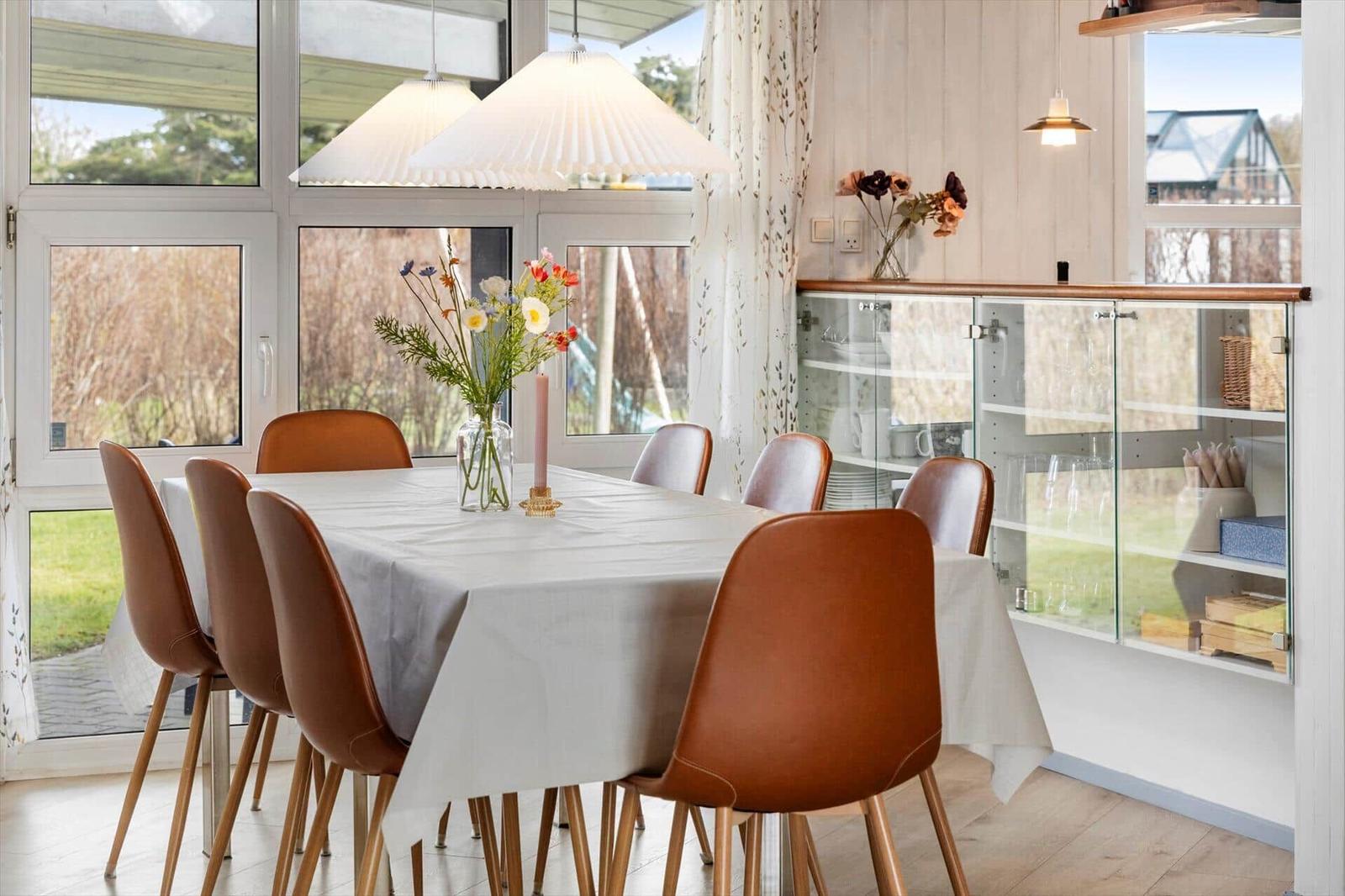 Esstisch mit sechs Stühlen, Blumenvase und Glasvitrine im Esszimmer.