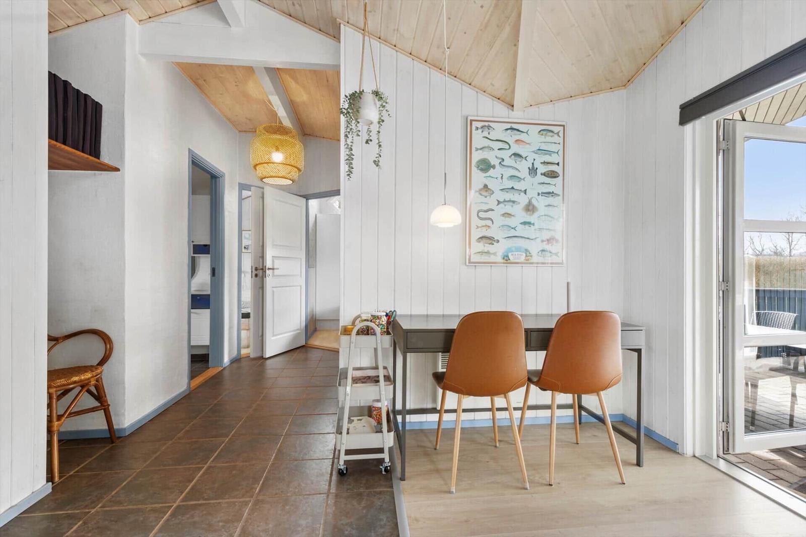 Essbereich mit Tisch, zwei Stühlen und Wandbild. Tür führt auf Balkon. Holzdecke und weiße Wände.