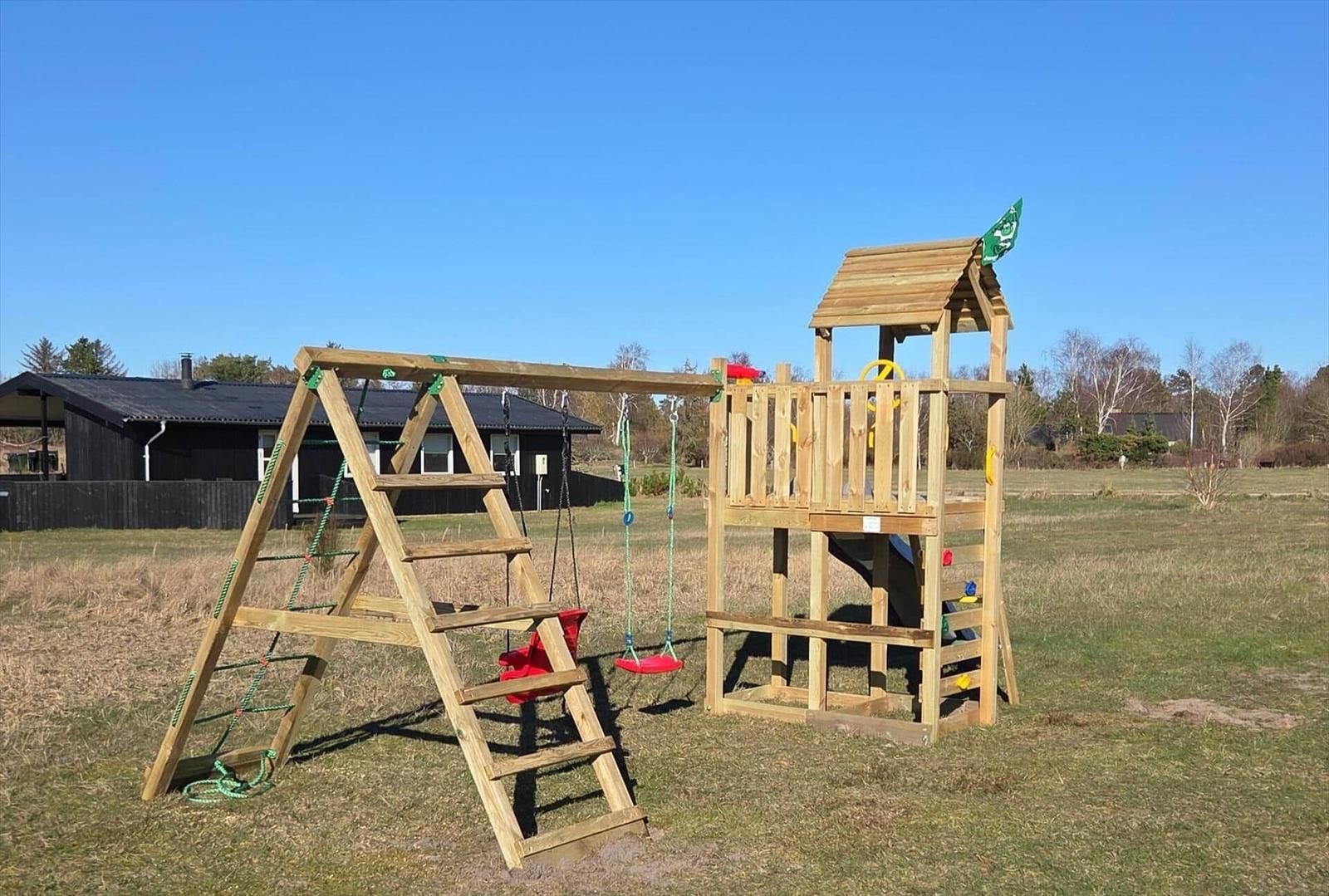 Holzspielplatz mit Klettergerüst, Rutsche und Schaukel im Gras.