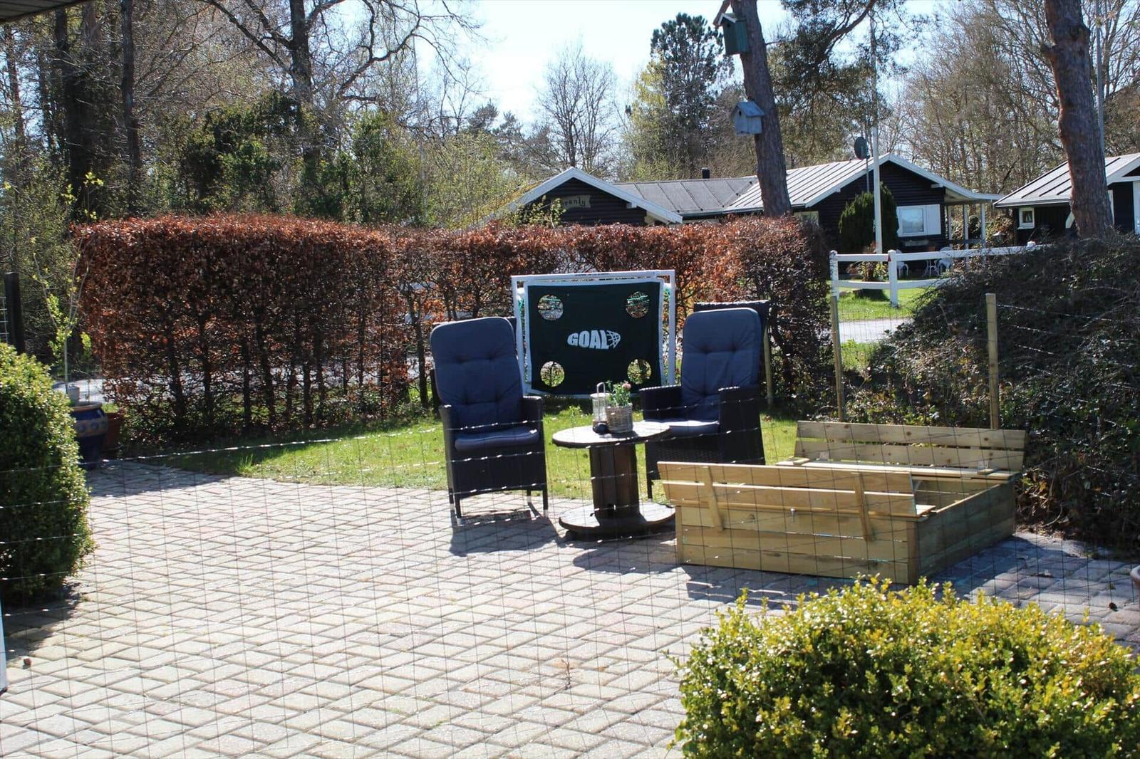 Terrasse mit zwei Sesseln, Tisch und Holzbeete. Hintergrund: Hecke und Häuser.