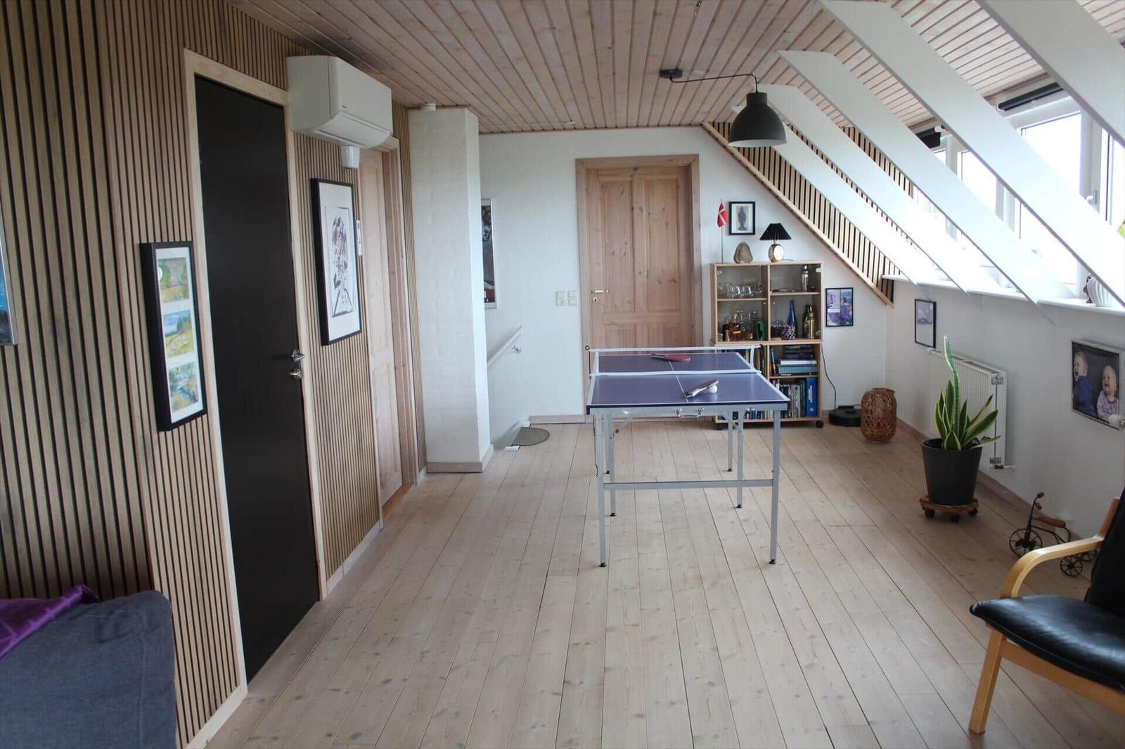Ein Raum mit Tischtennisplatte, Holzboden und Treppe zur oberen Etage.