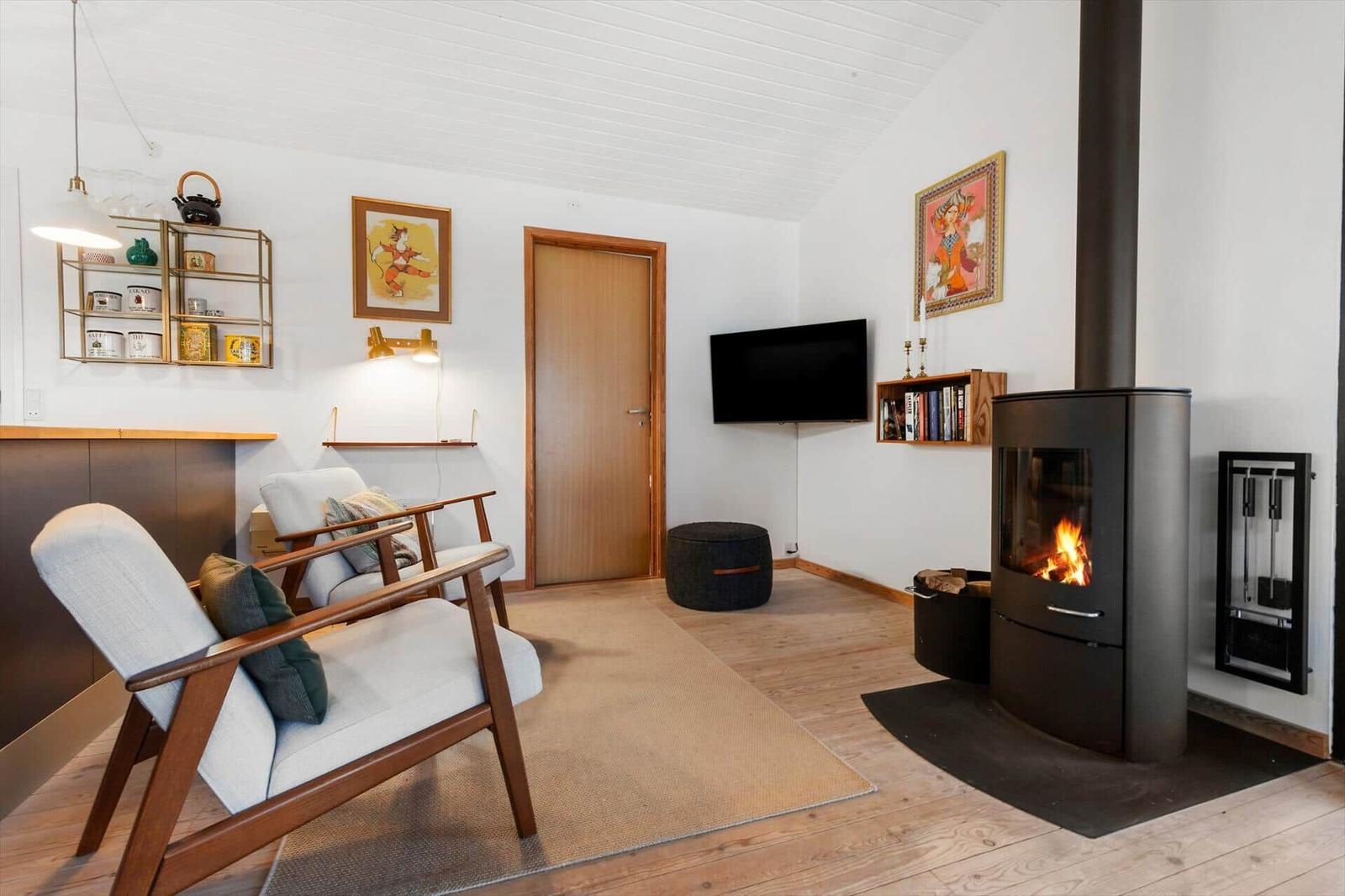 Wohnzimmer mit Kamin, Fernseher und zwei Sesseln auf Holzboden.