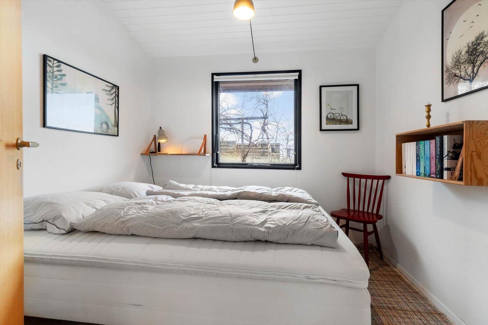Schlafzimmer mit Bett, Fenster und Wandregal mit Büchern.