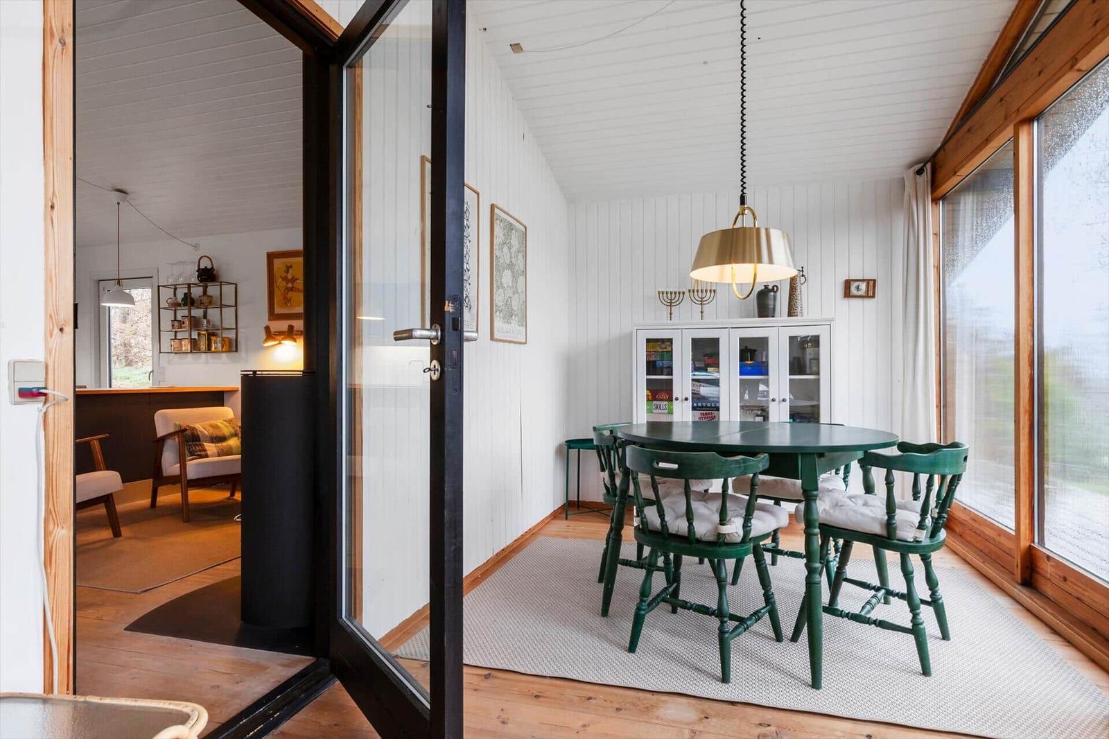 Esszimmer mit grünem Tisch und Stühlen, Glasfront und weißen Wänden.