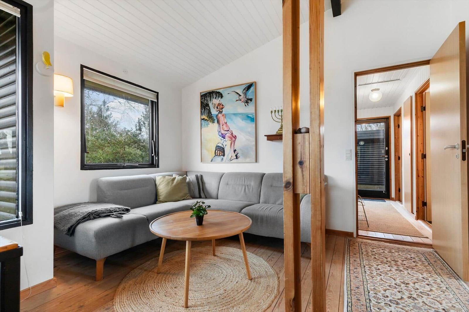 Wohnzimmer mit grauem Sofa, runden Tisch und Wandbild. Holzfußboden und Tür zur Eingangshalle.