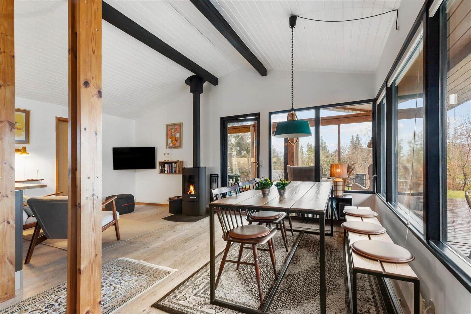Essbereich mit Tisch, Stühlen und Fensterblick. Im Hintergrund Wohnzimmer mit Kamin und Fernseher.