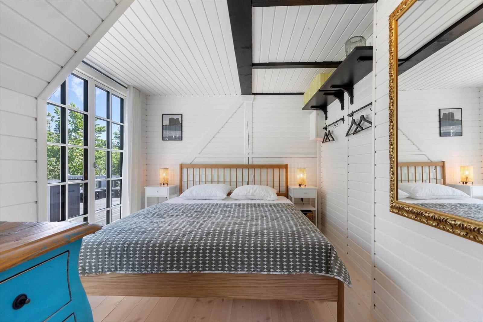 Schlafzimmer mit Dachschräge, großem Fenster und Holzbett. Spiegel und Kleiderständer sind vorhanden.