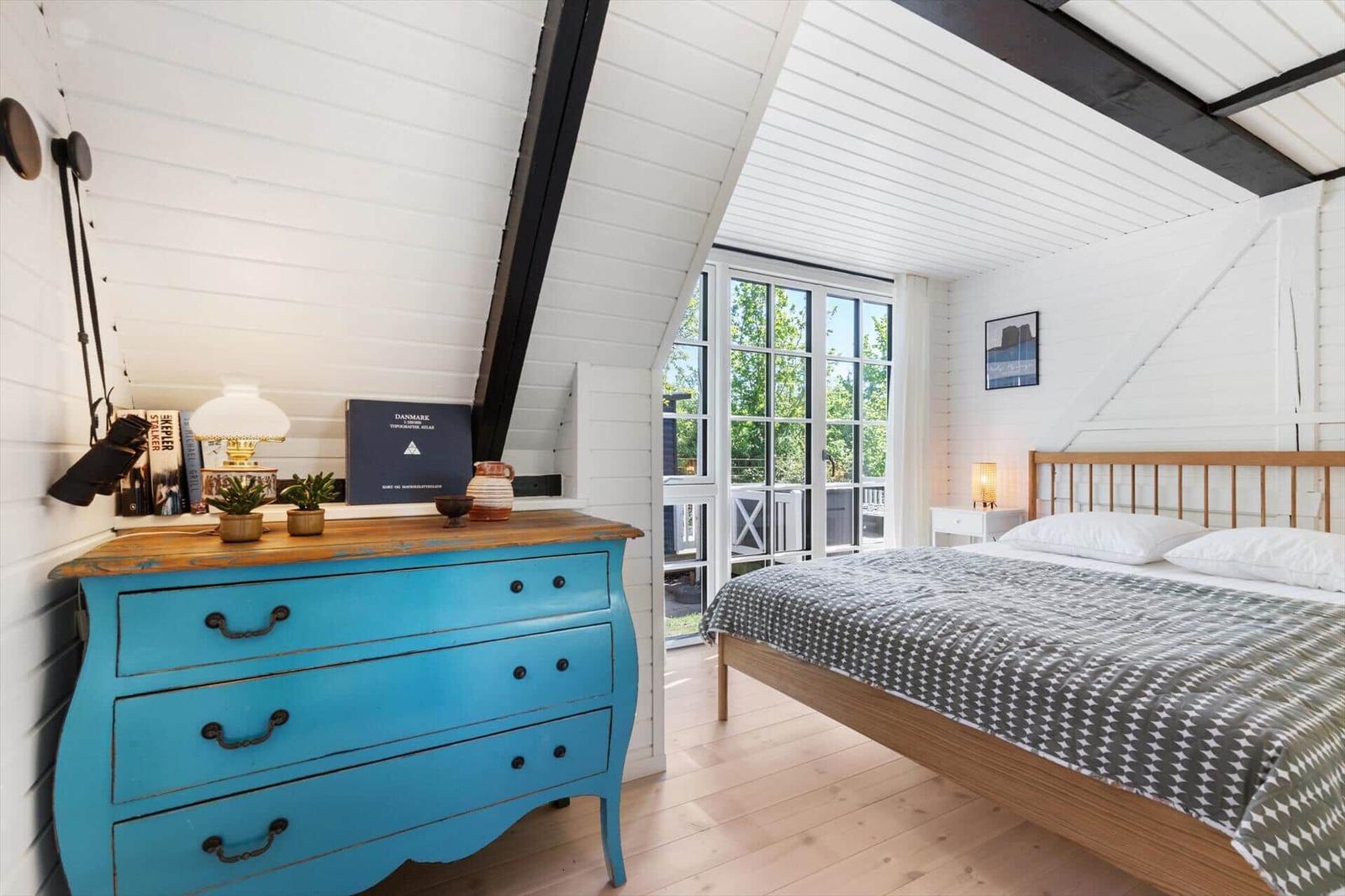 Schlafzimmer mit Holzboden, blauem Schrank und Bett unter schrägem Dach