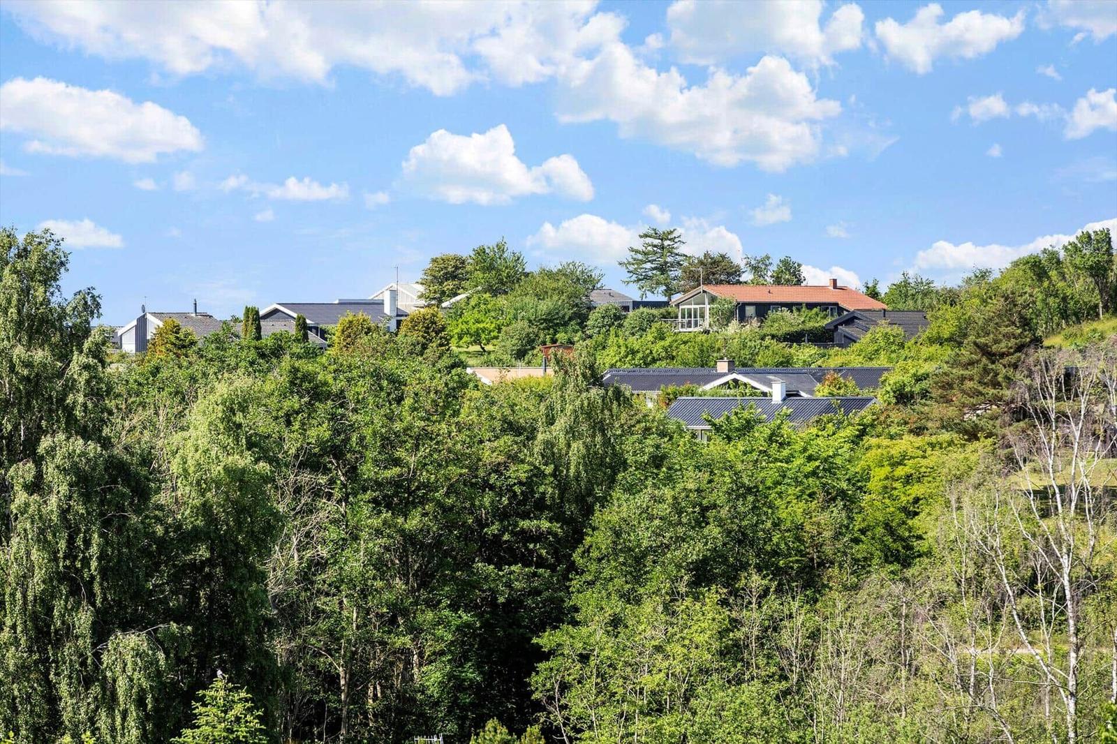 Häuser auf Hügeln umgeben von grüner Vegetation unter blauem Himmel mit weißen Wolken.
