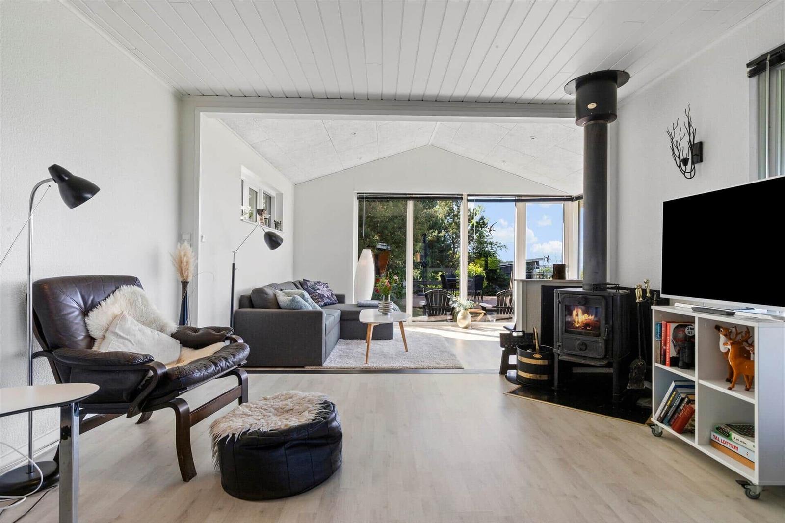 Wohnzimmer mit Kamin, Sofa, Sessel und Fernseher. Durchgang zur Terrasse mit Gartenansicht.