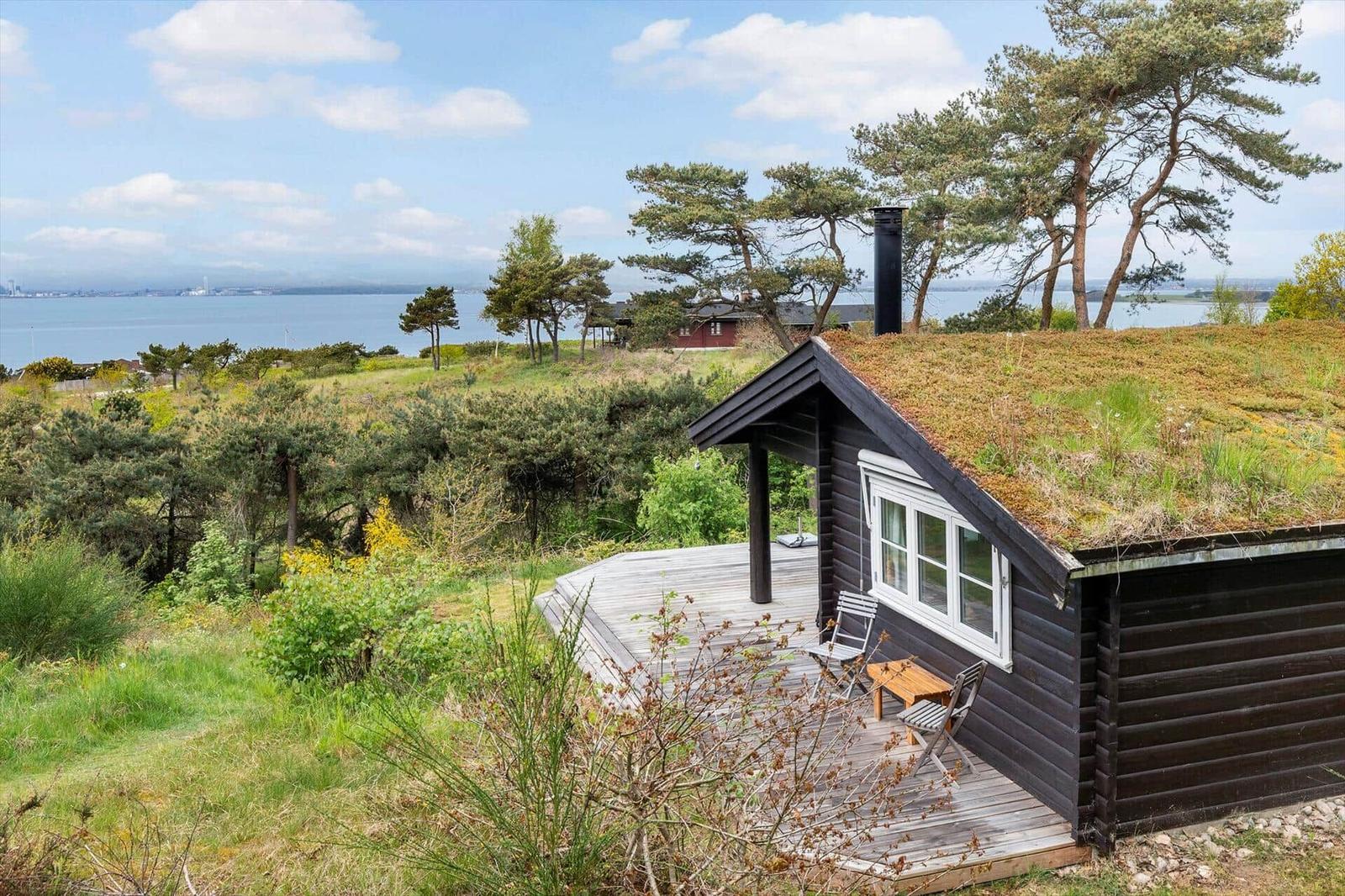 Hütte mit Grasdach und Holzterrasse, Blick auf Wasser und Bäume.