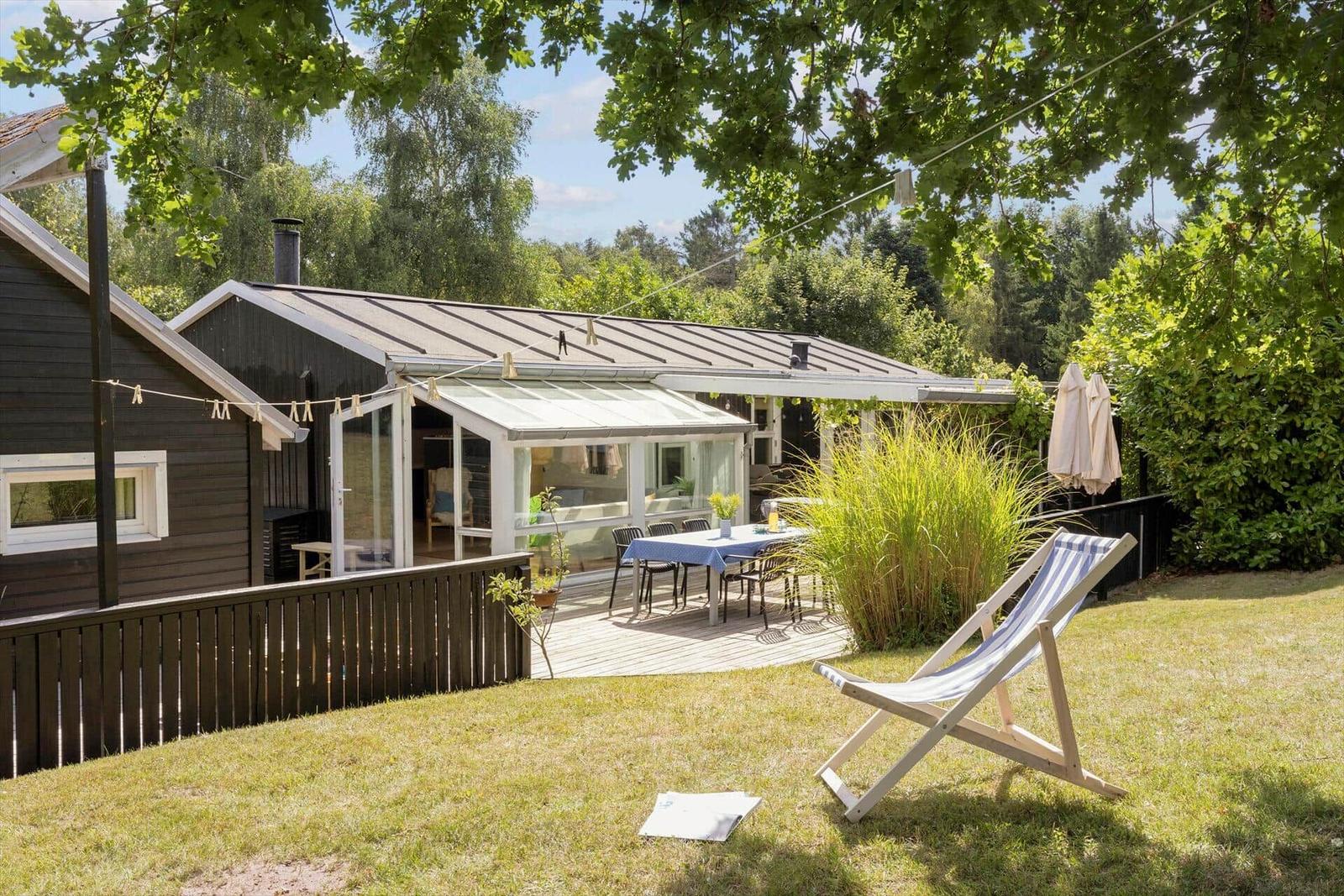 Haus mit Terrasse, Garten und Liegestuhl unter Bäumen.