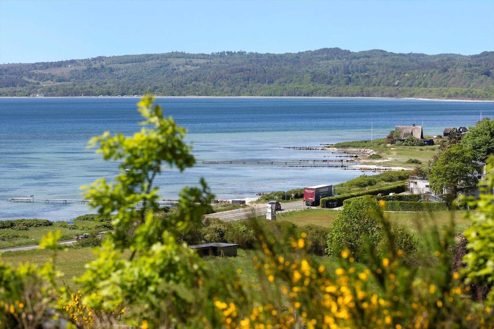 View of a lake with green hills and a shoreline road with vehicles.