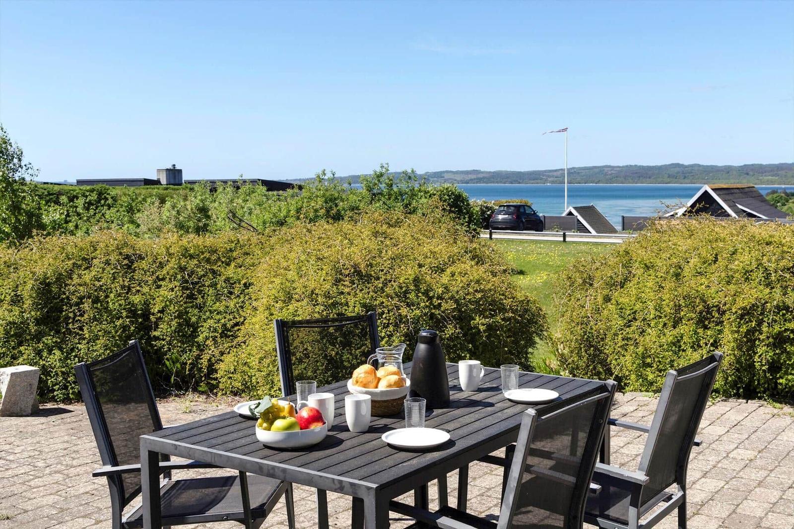 Outdoor table with chairs, fruit, and drinks. View of water and green areas.