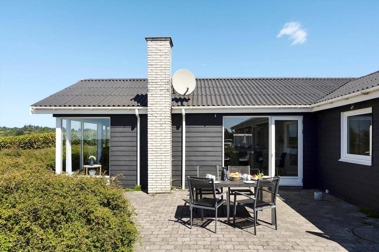 Modern villa with terrace, seating group, and satellite dish. Dark facade and white chimney.