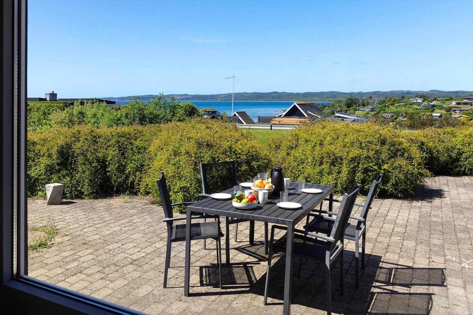 Terrace with table and chairs, view of sea and green hedge.