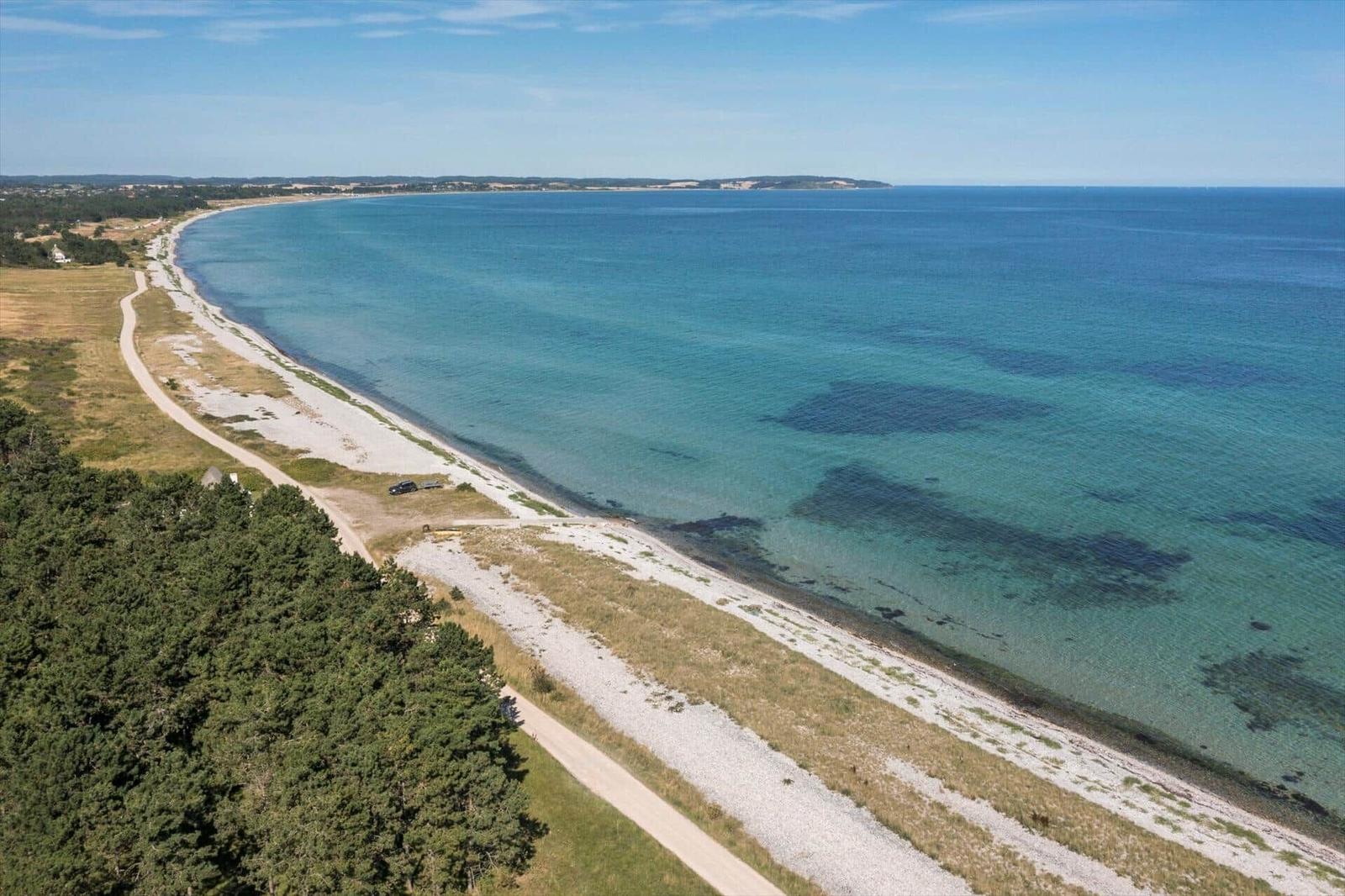Ausblick auf Strand mit Sandstrand und klarer See. Wald und unbefestigte Straße entlang.