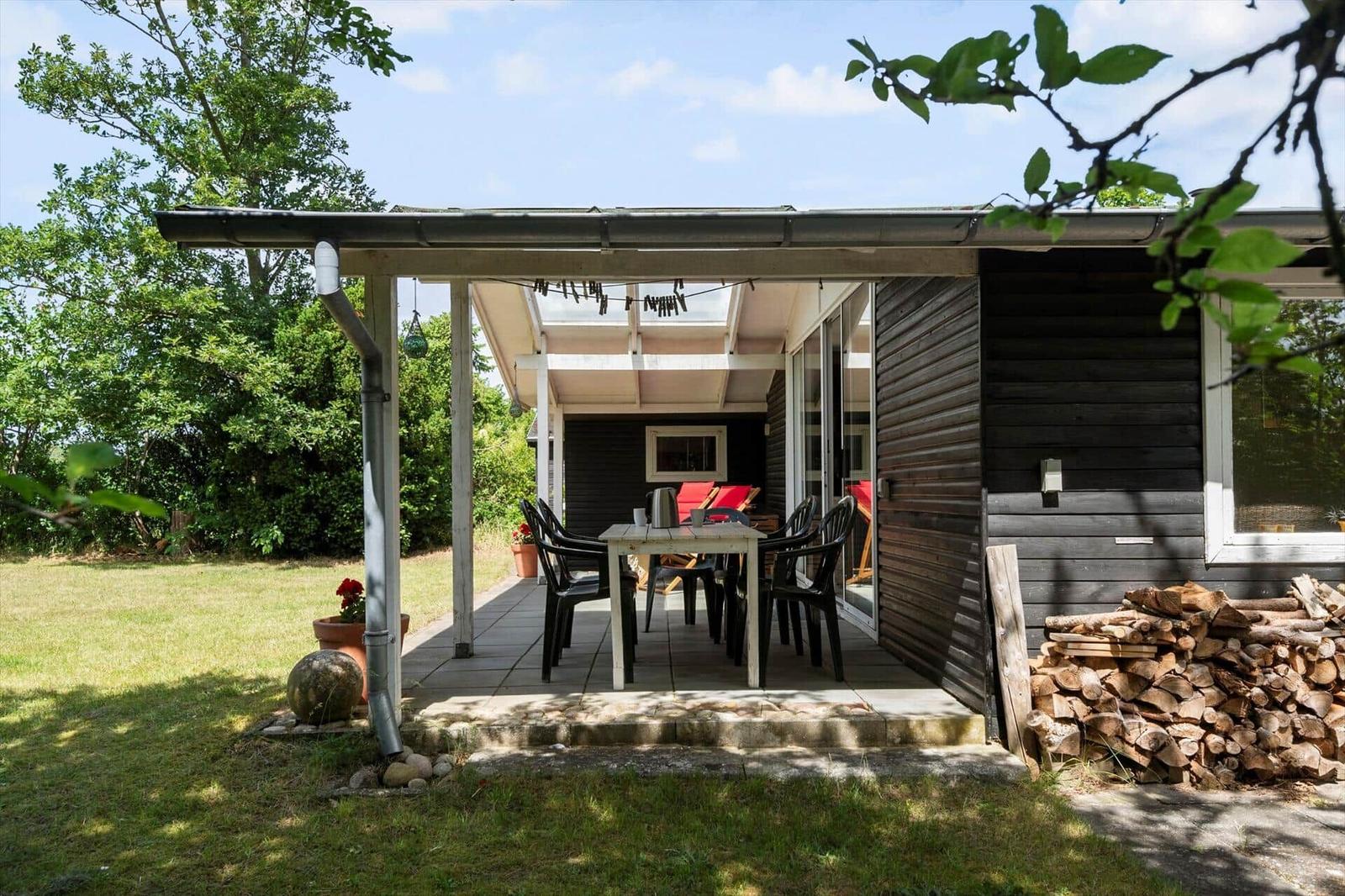 Terrasse mit Tisch und Stühlen, Holzstapel und grünem Gartenbereich.