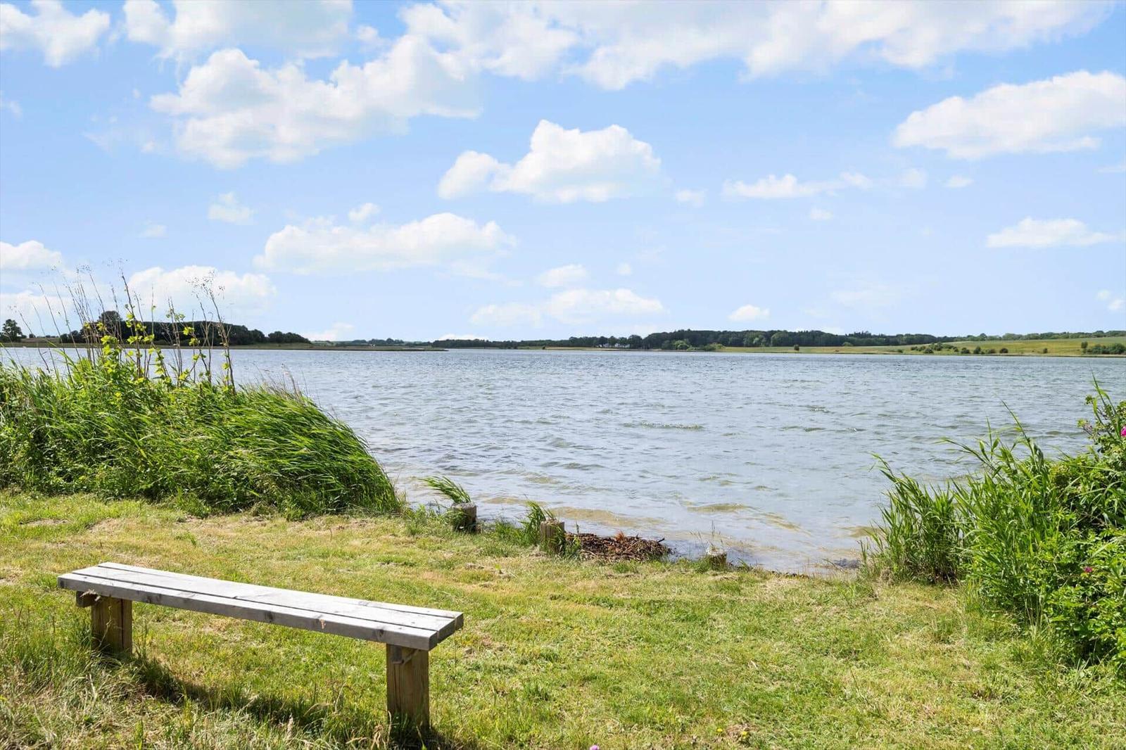 Holzbank am Ufer eines Sees mit Blick auf die gegenüberliegende Uferseite.