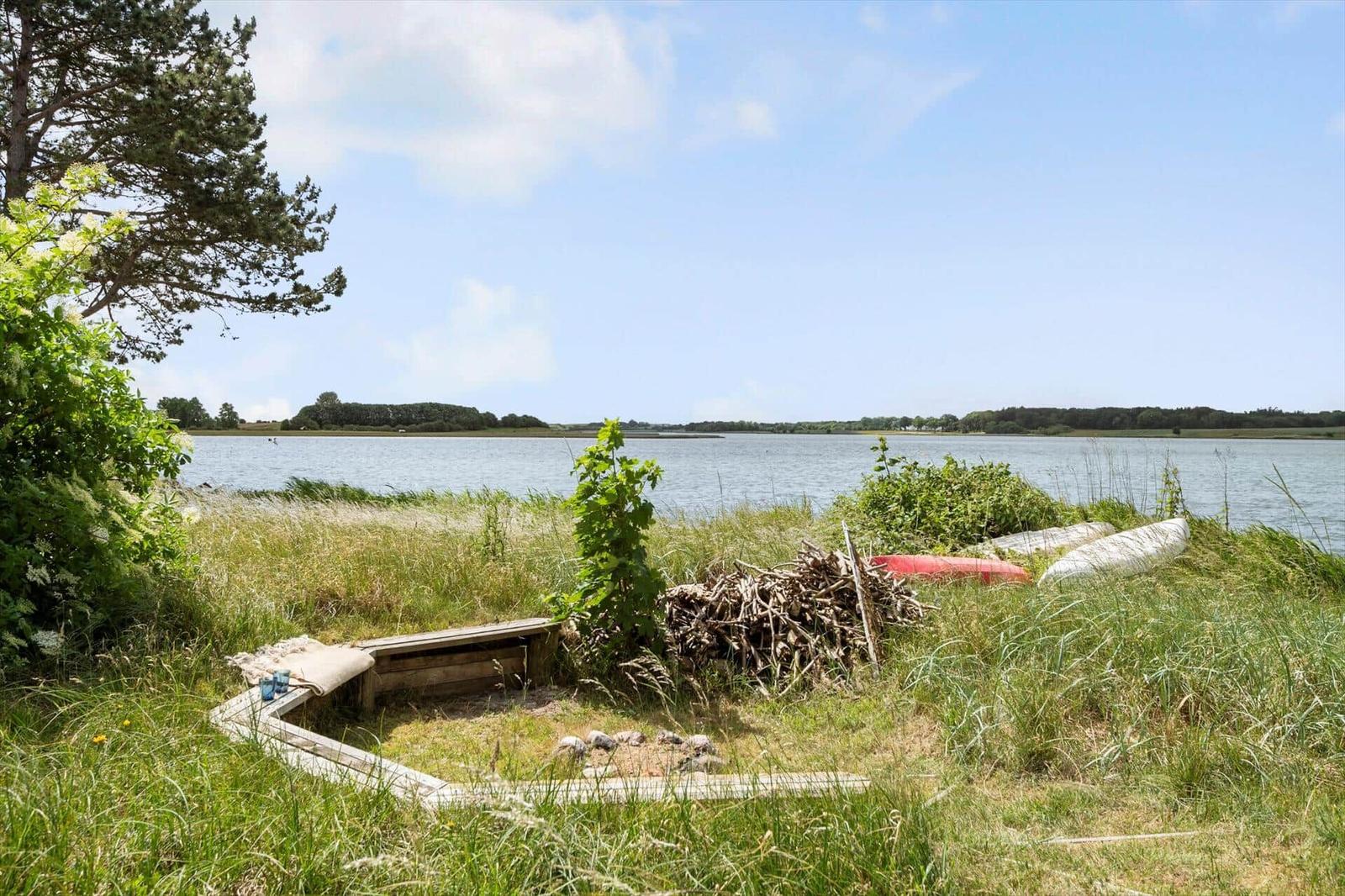 Grünes Ufer mit Kanu, Feuerstein und Holzstapel am Wasser
