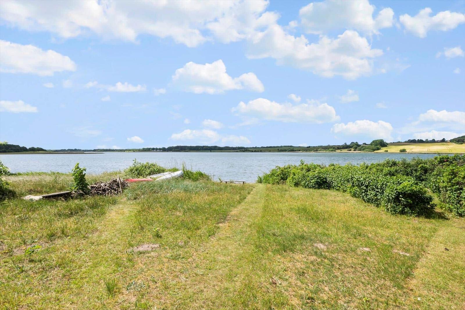 Grasfläche mit Blick auf einen See unter blauem Himmel mit weißen Wolken.