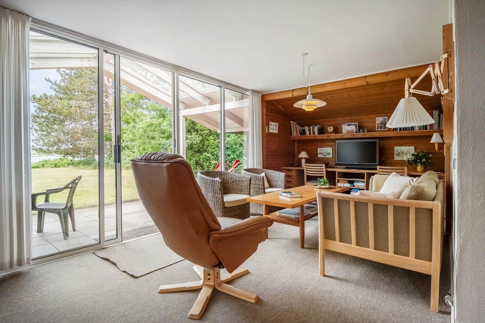 Wohnzimmer mit braunem Ledersessel, Holzmöbel und Glasfront zur Terrasse.