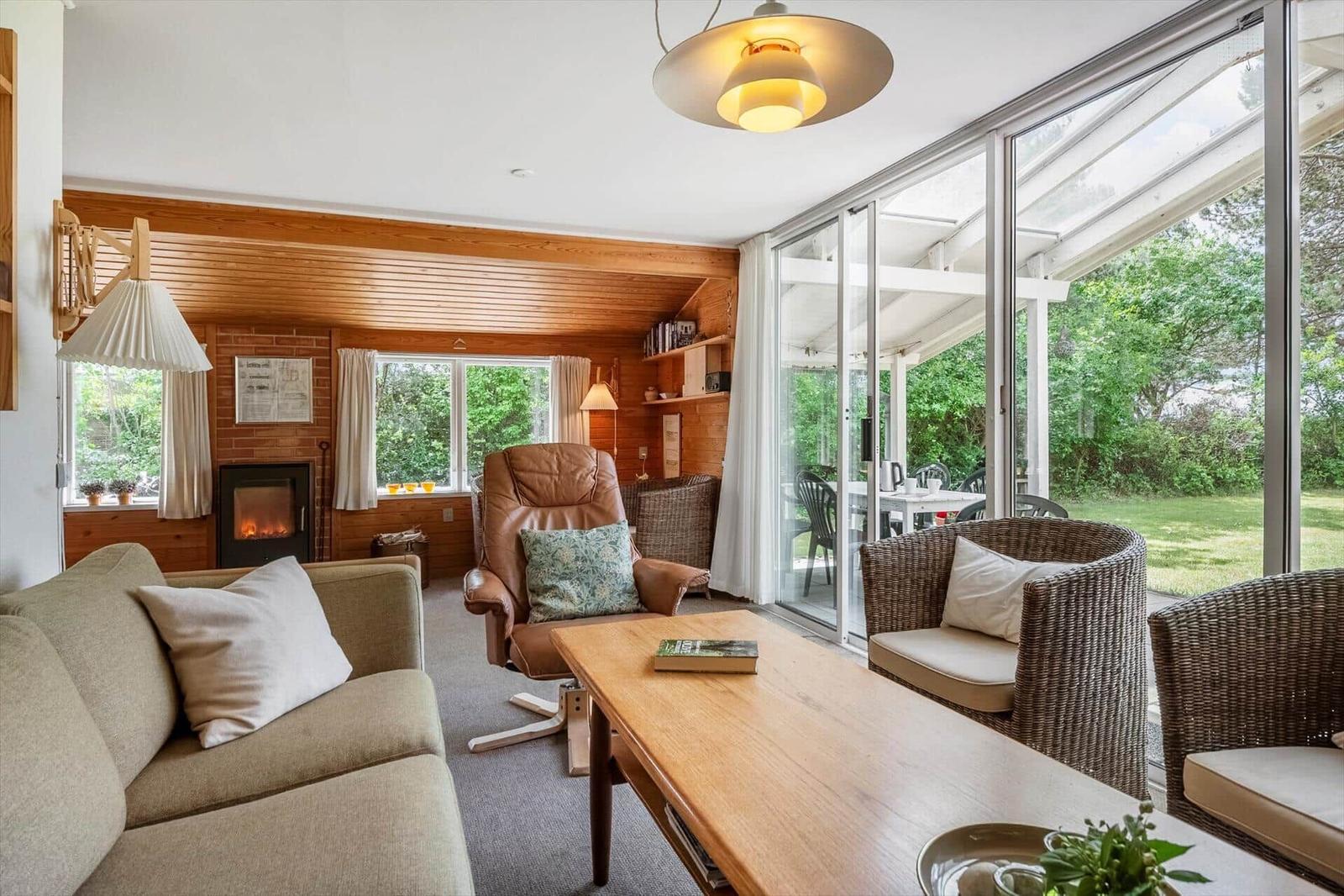 Wohnzimmer mit Sofa, Sessel und Tisch. Durchgang zu Terrasse mit Gartenansicht.