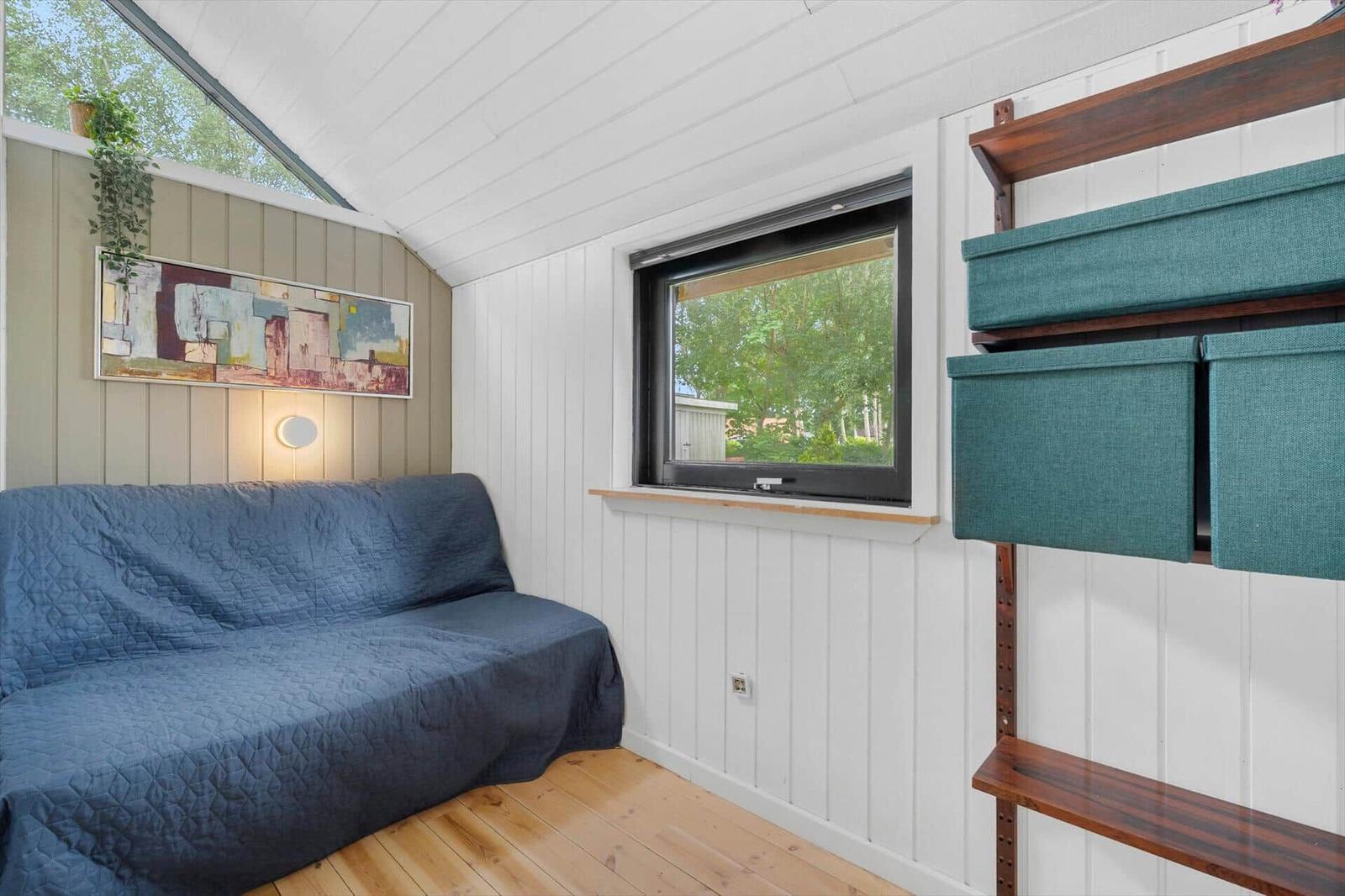 Ein Raum mit Sofa, Fenster und Regal. Holzfußboden und weiße Wände.