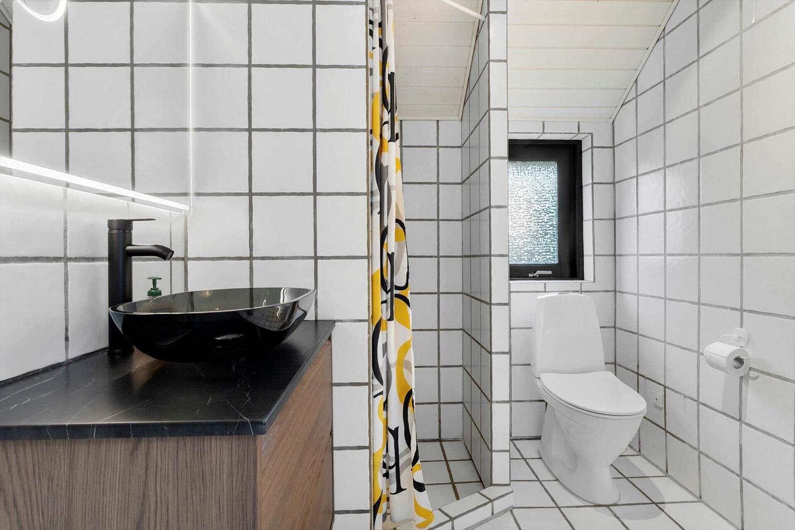 Badezimmer mit Waschbecken, Toilette und Dusche. Fliesenwand und schwarzer Waschtisch.