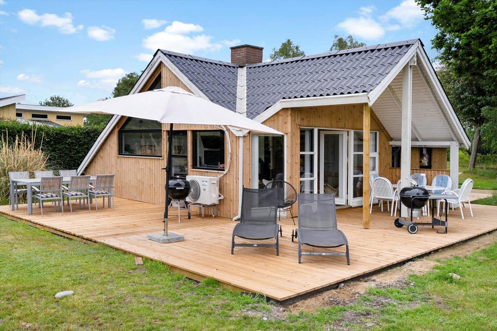 Holzhaus mit Terrasse, Grill und Sitzgelegenheiten im Freien.
