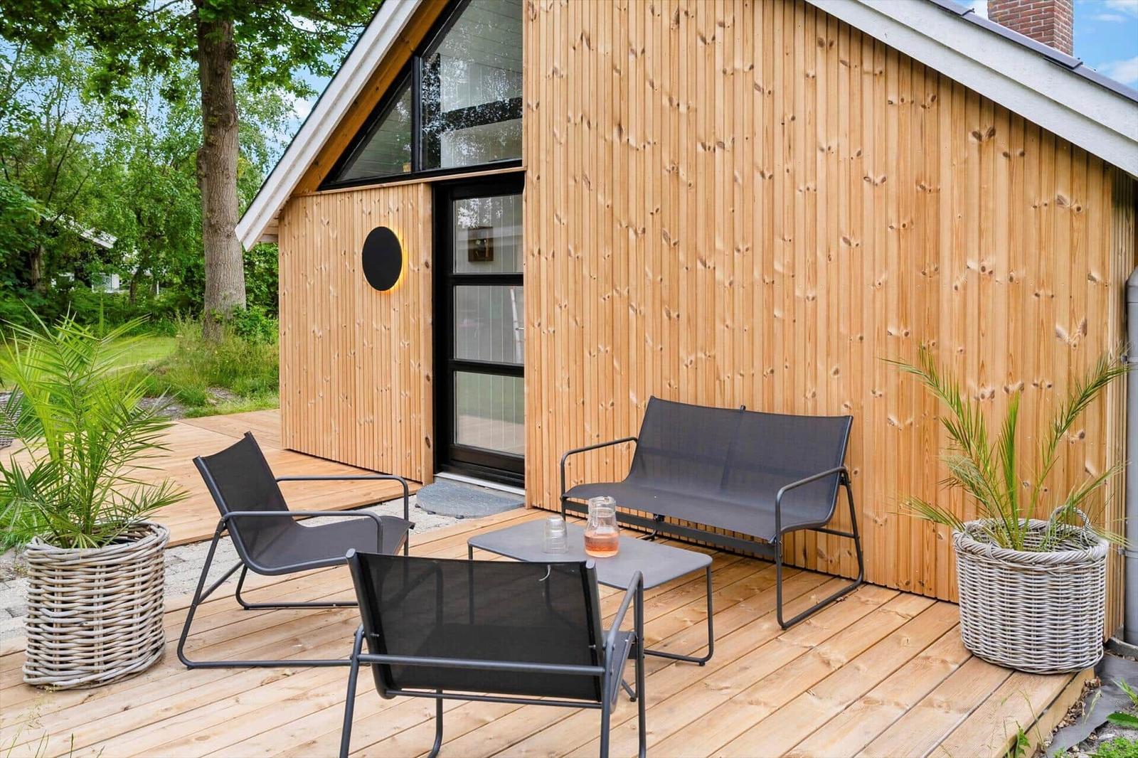 Terrasse mit Sitzgruppe und Pflanzen vor einem Holzhaus mit Glasfront.