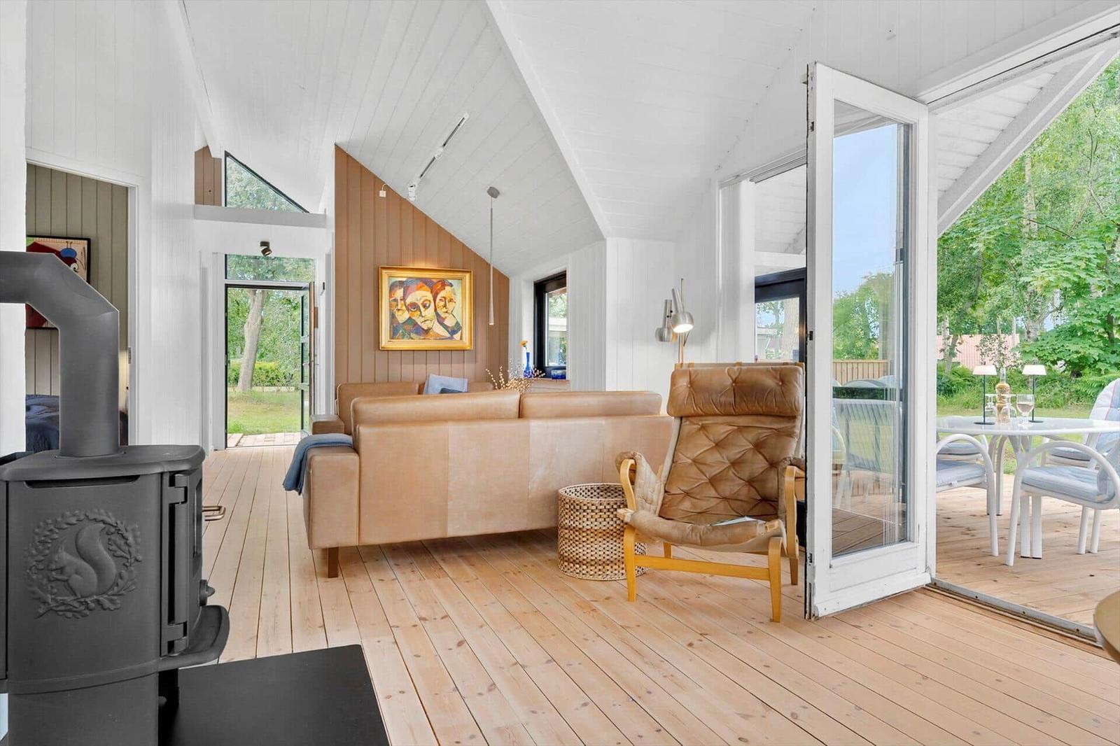 Wohnzimmer mit Sofa, Sessel und Kamin. Terrasse mit Tisch und Stühlen. Holzboden und weiße Wände.