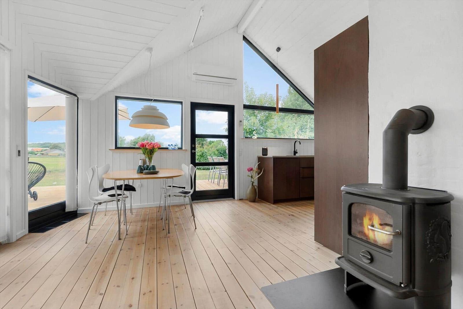 Raum mit Esstisch, Kamin und großem Fenster. Holzboden und weiße Wände.