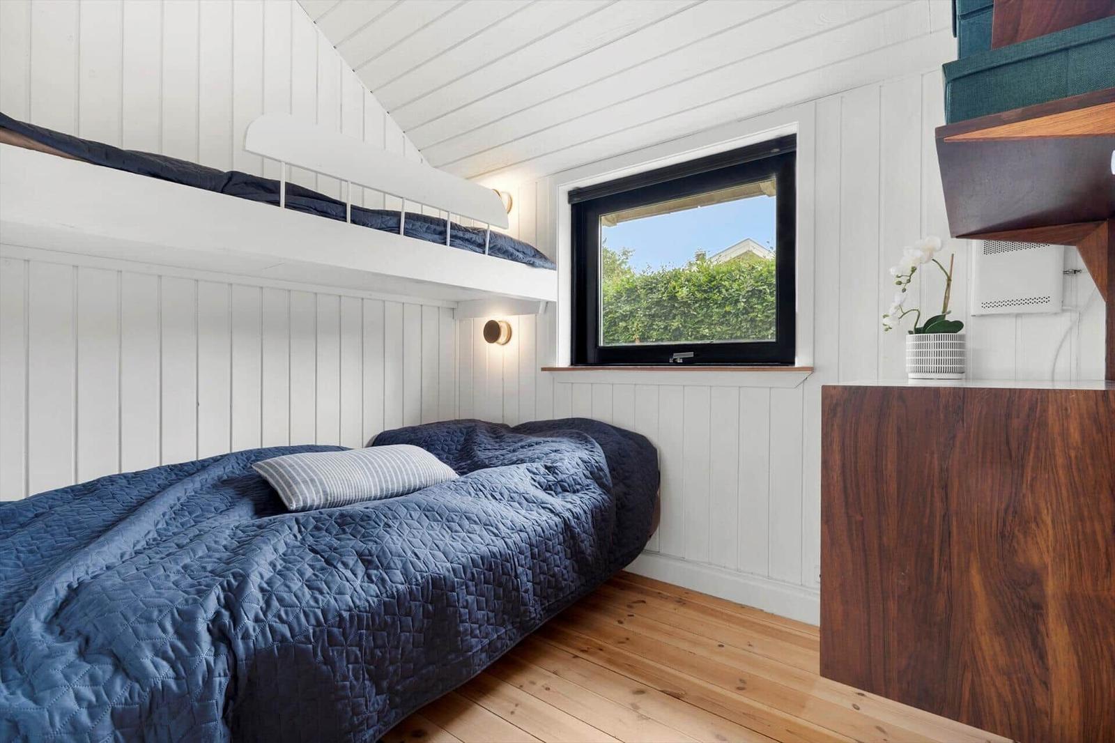 Schlafzimmer mit Doppelbett und Hochbett, Holzboden und Fenster mit Blick auf Grün.