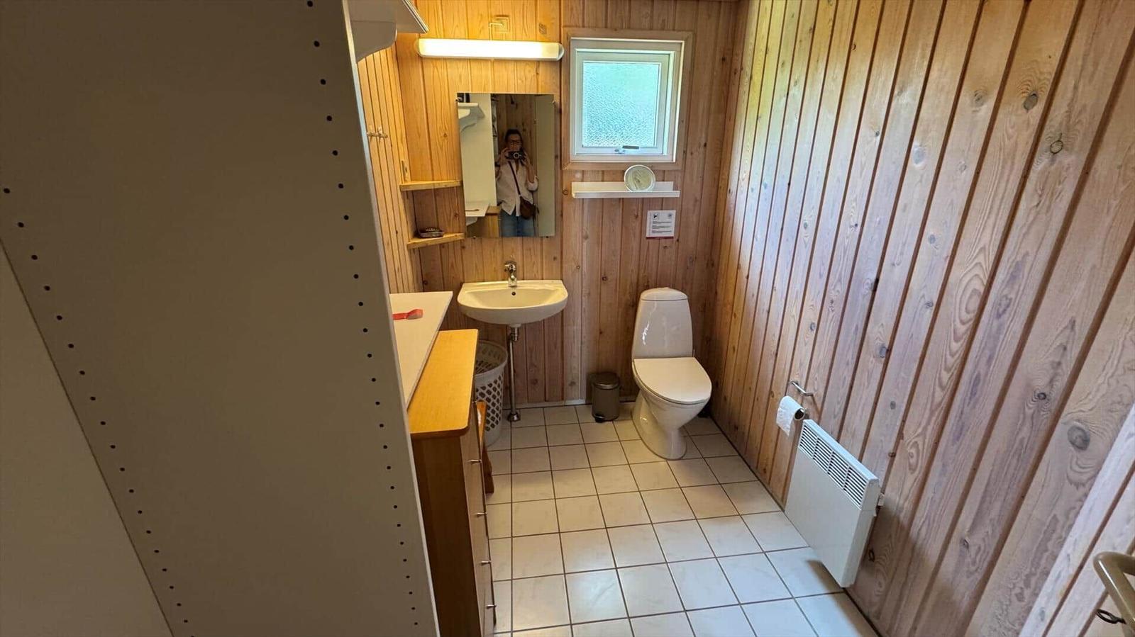 Badezimmer mit Toilette, Waschbecken und Spiegel an Holzwand