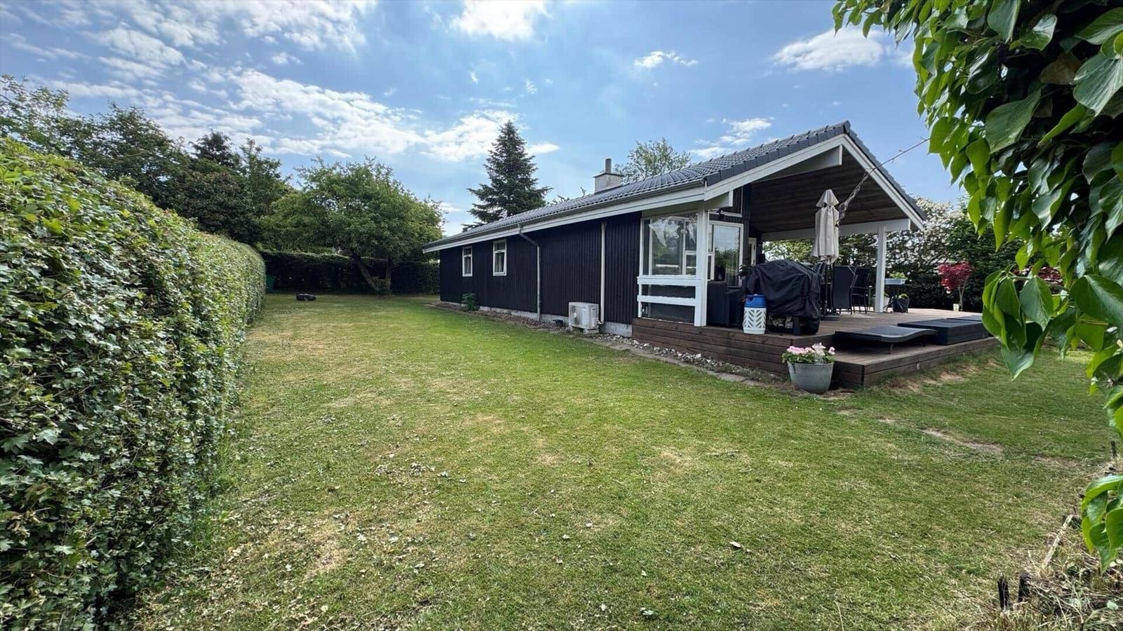 Schwarzes Haus mit Terrasse und Garten. Grill, Sonnenliegen und Pflanzen sind vorhanden.