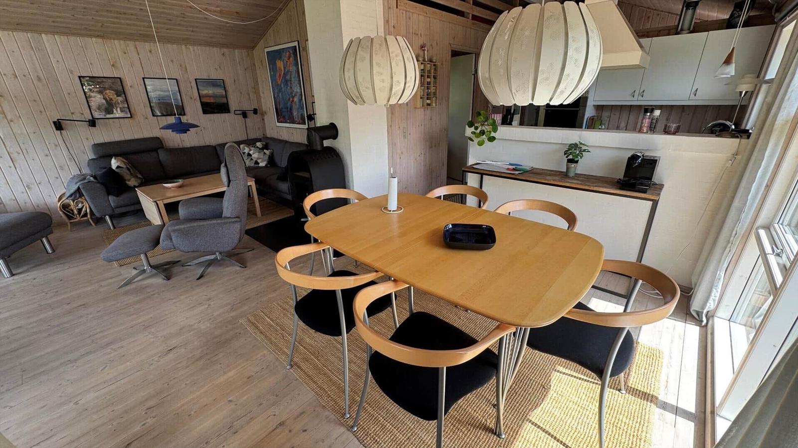 Essbereich mit Holztisch und Stühlen, Küche und Wohnzimmer im Hintergrund.