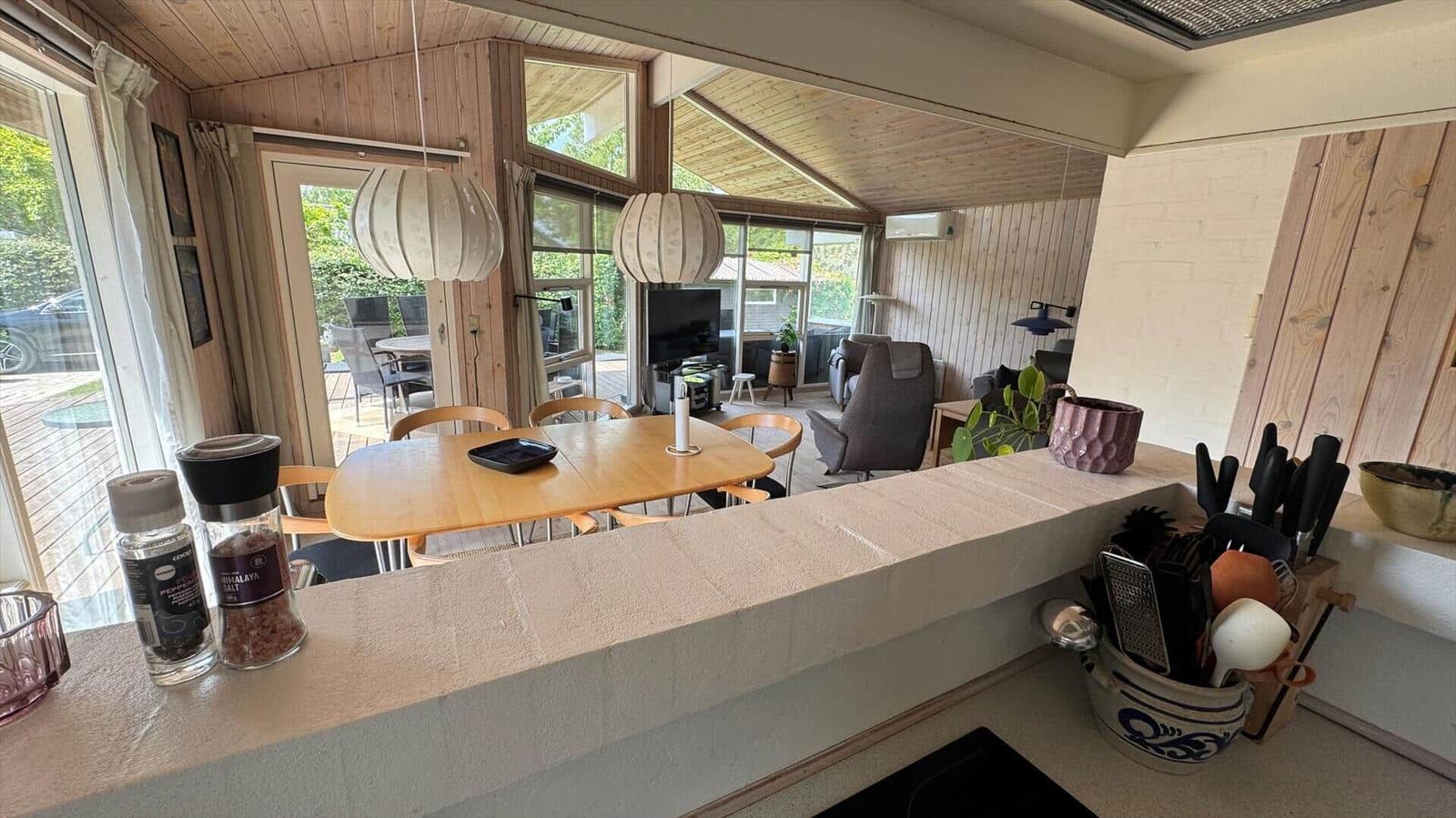 Küche mit Essbereich und Blick in Wohnzimmer mit Holzwänden und großen Fenstern.