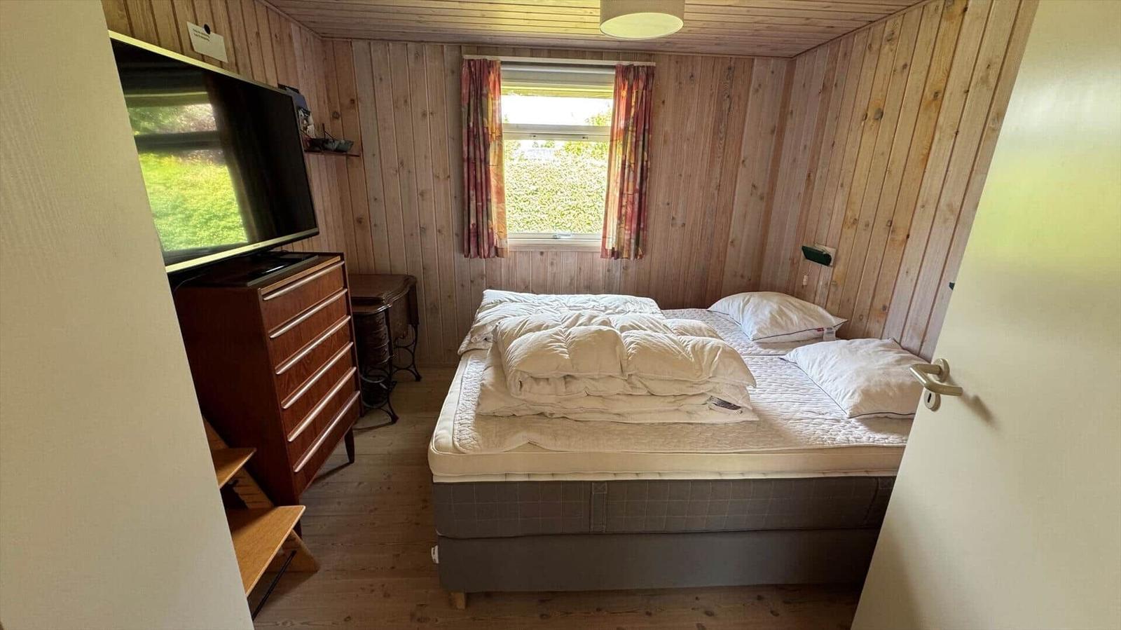 Schlafzimmer mit Holzwand, Bett, Fenster und Fernseher.