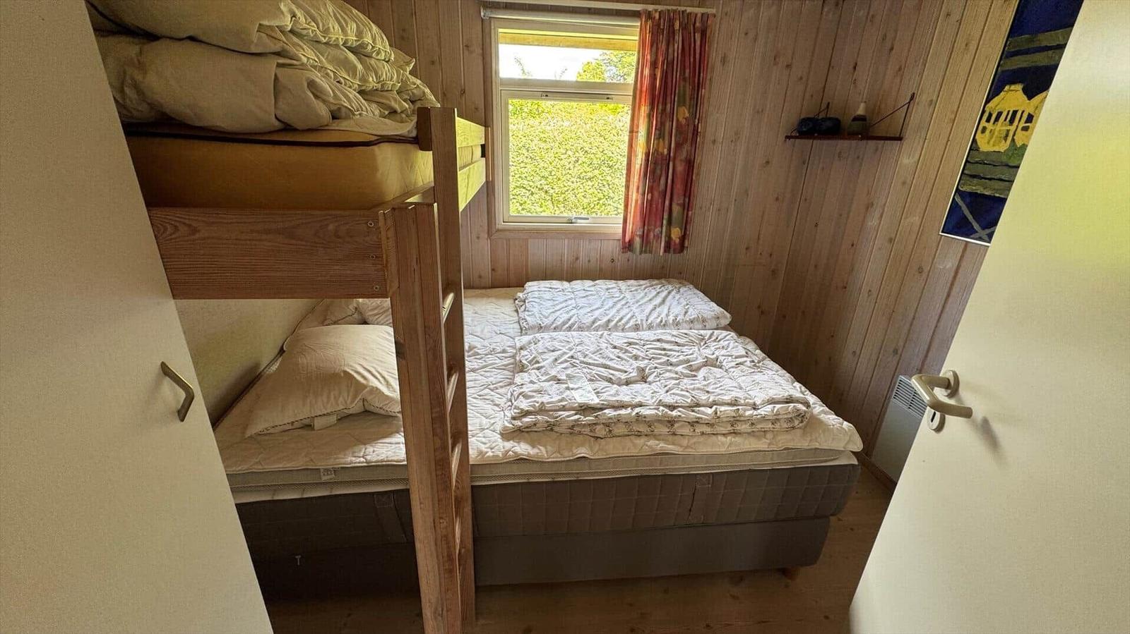 Zimmer mit Doppelbett und Schlafcouch, Holzwand, Fenster mit Vorhang.