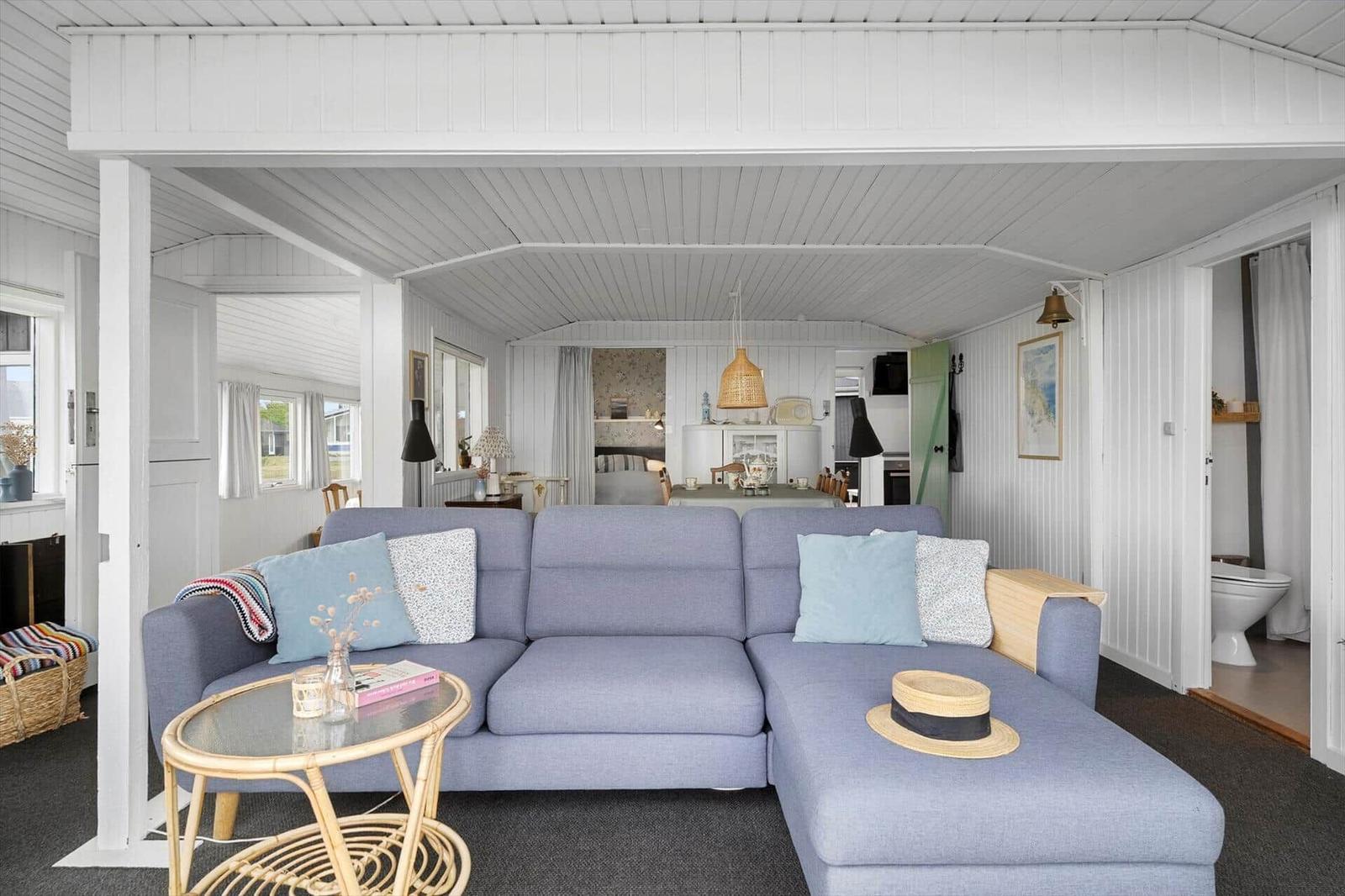 Ein Wohnzimmer mit blauem Sofa, Glas-Tisch und Blick in die Küche.
