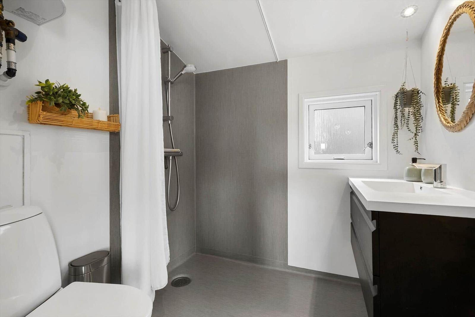 Badezimmer mit Dusche, Waschbecken und Toilette. Weiße Wände und graue Fliesen.