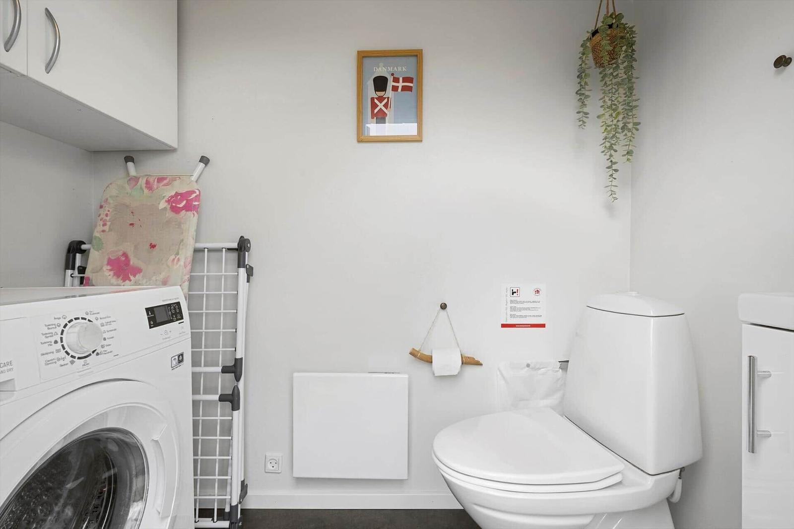 WC mit Waschmaschine, Heizkörper und Wandbild mit dänischer Flagge.
