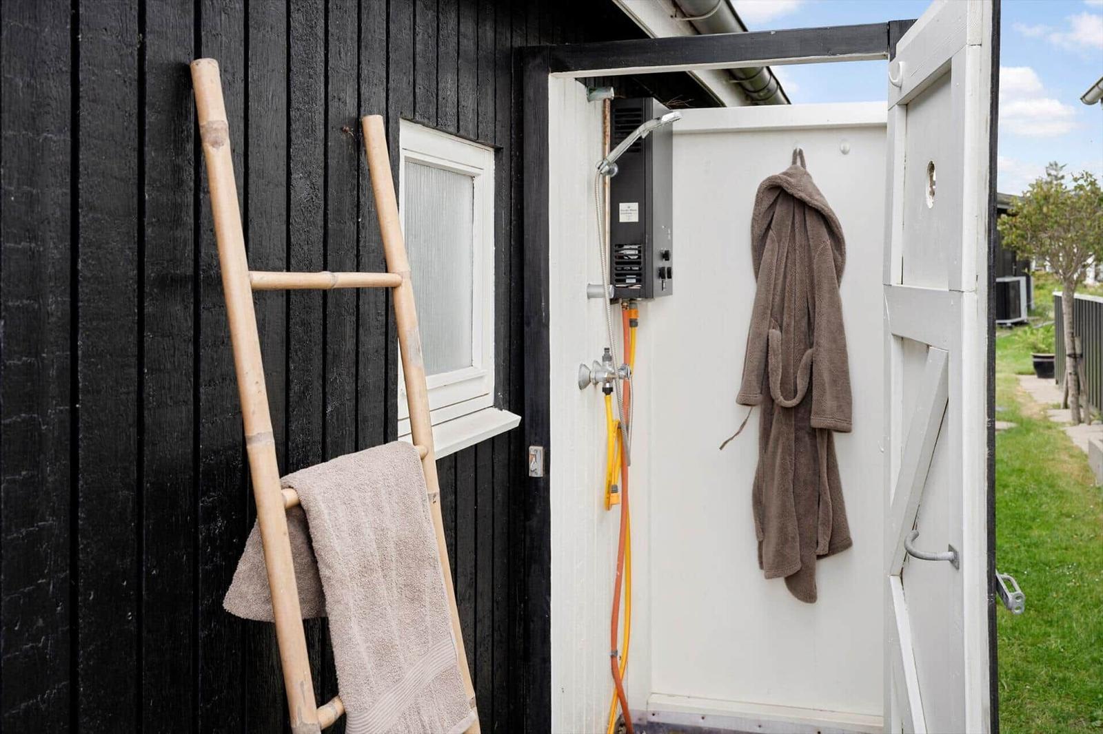 Außen-Dusche mit Brause, Handtuch und Bademantel an der Wand.