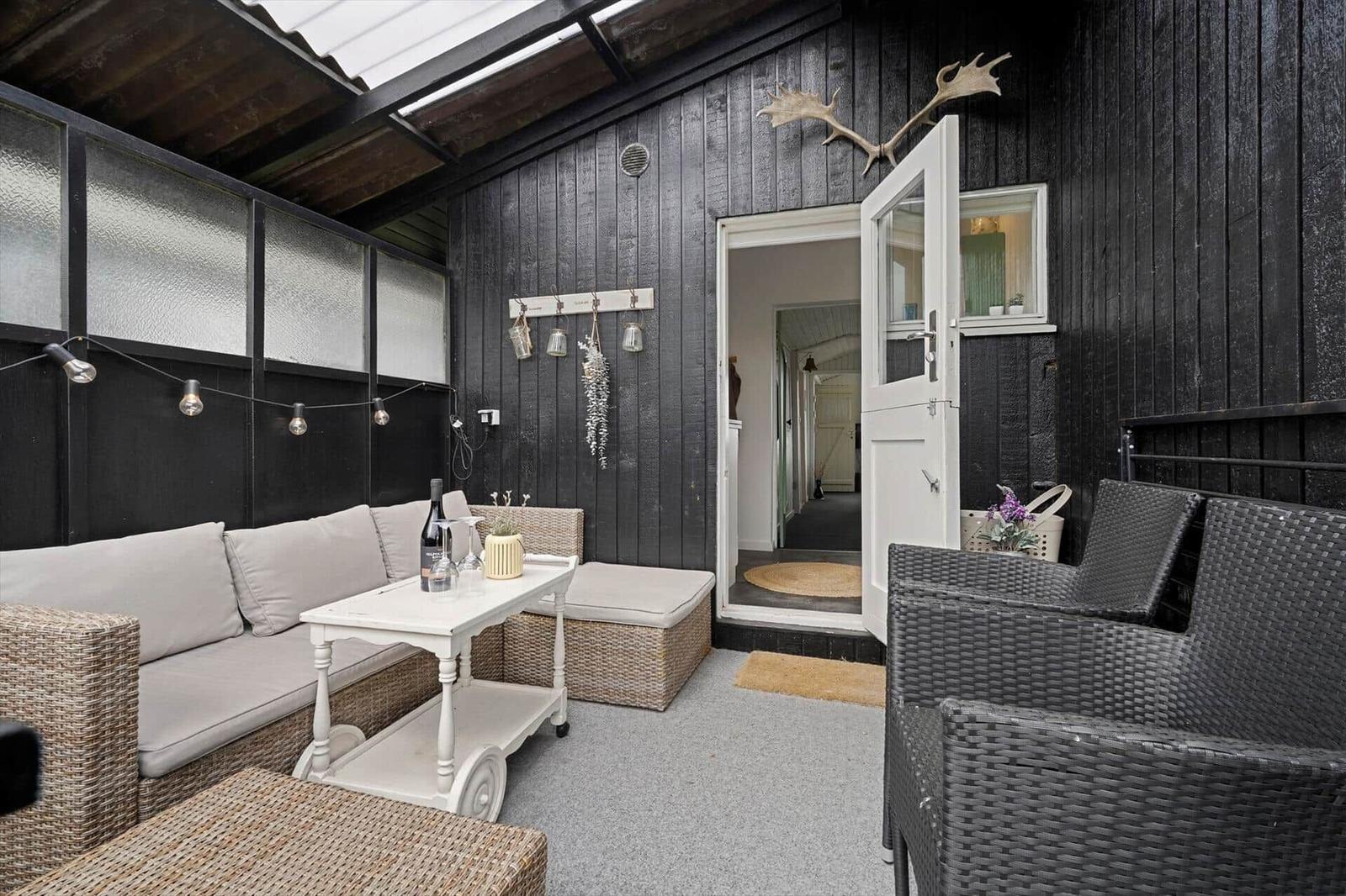Terrasse mit Sitzgruppe, Tisch und Eingangstür. Schwarze Holzwände und Decke.