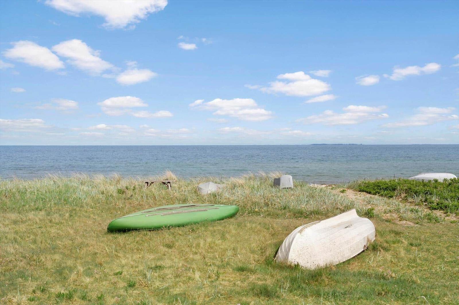 Zwei Boote liegen auf Gras am Strand. Im Hintergrund das Meer und blauer Himmel.