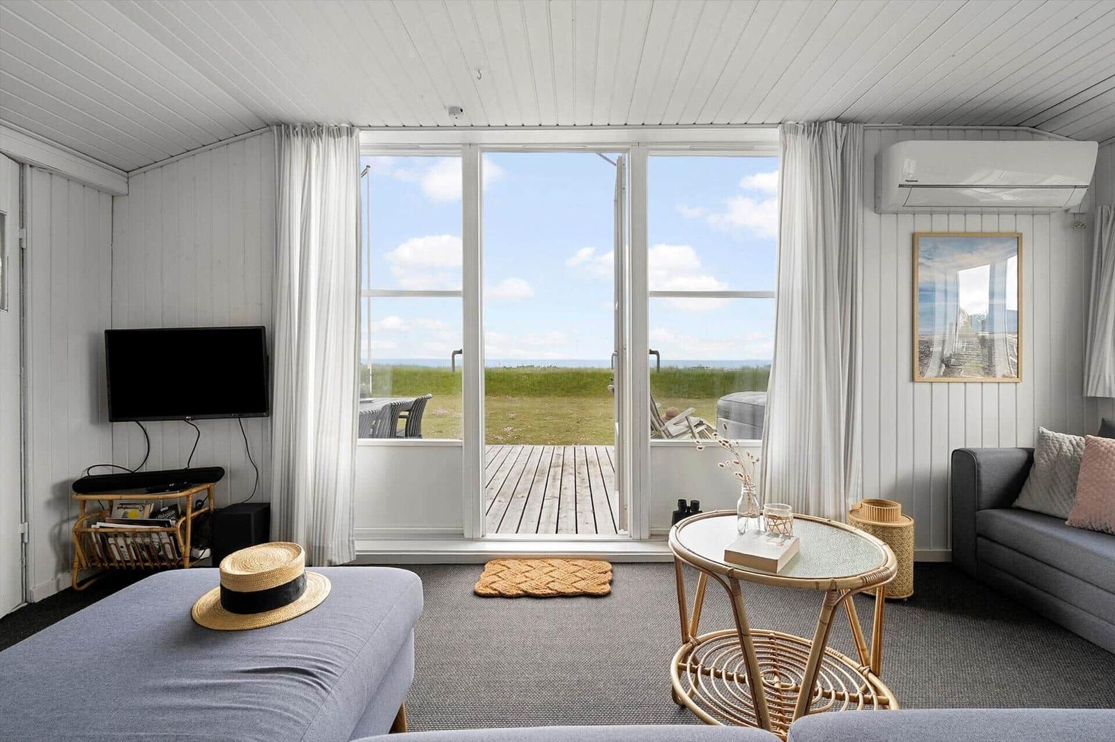 Wohnraum mit Fernseher, Sofa und Blick auf Terrasse und Landschaft.