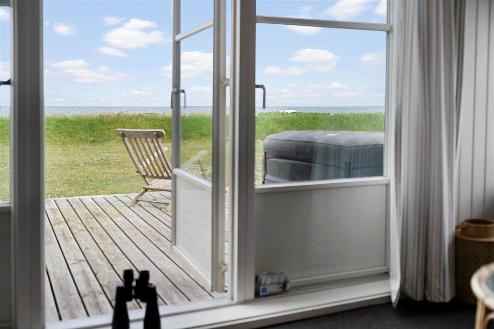 Durch die offene Tür blickt man auf eine Terrasse mit Stuhl und Hot Tub am Meer.